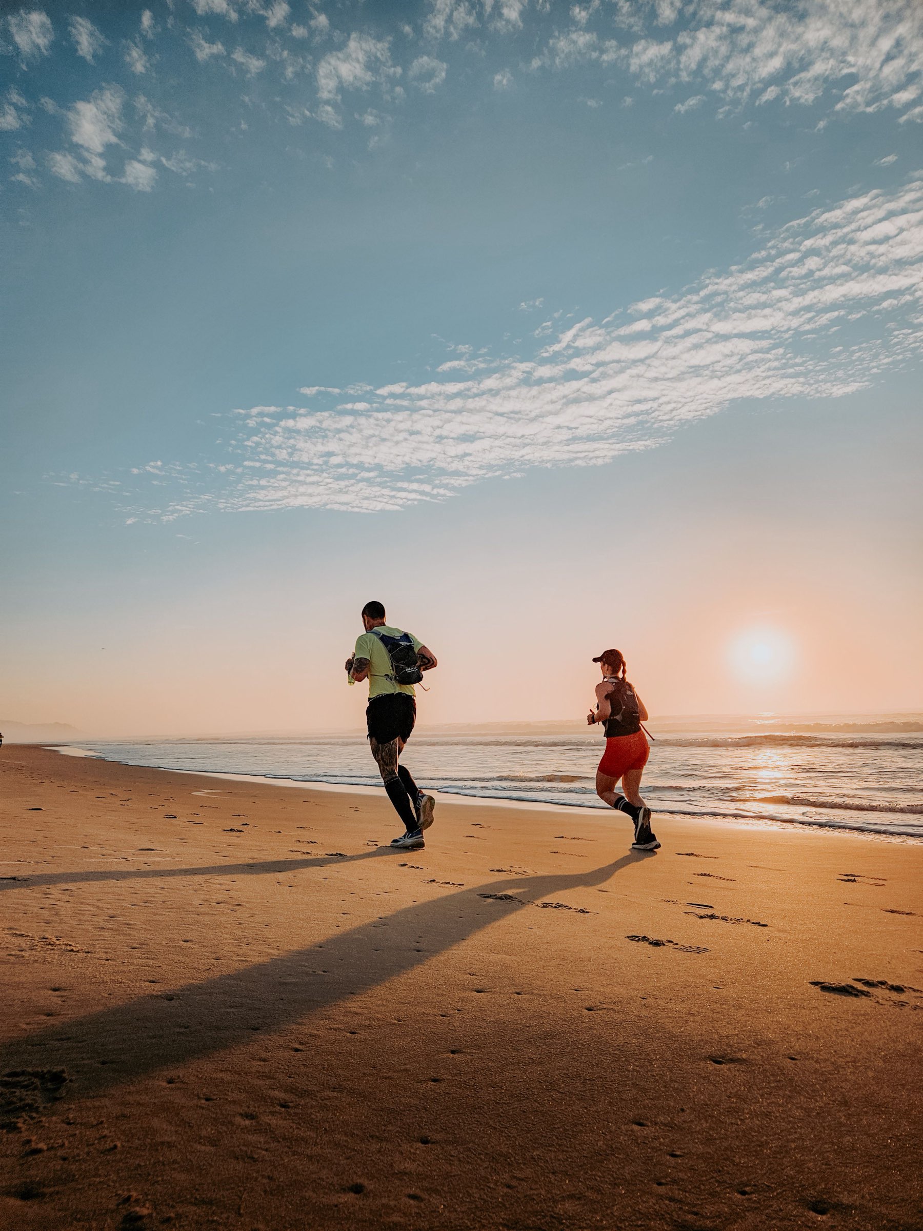 Zwei Läufer joggen bei Sonnenaufgang am Strand entlang der Wasserkante